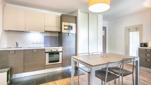 A modern kitchen with a built-in oven, microwave, and a dining area with a table and chairs. - Flat with a balcony near the slopes (Les Deux Alpes)