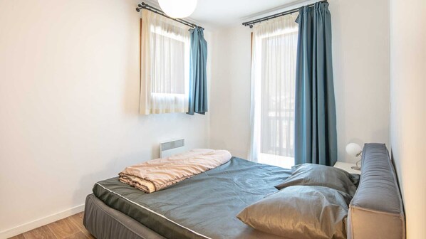 A bedroom with a bed, a bedside table, a lamp, and a window with curtains.