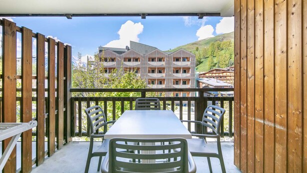 A balcony with a table and chairs, overlooking a building with a modern design and a mountainous backdrop. - Flat with a balcony near the slopes (Les Deux Alpes)