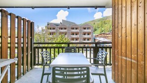 A balcony with a table and chairs, overlooking a building with a modern design and a mountainous backdrop.