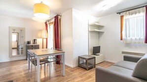 A modern living room with a sofa, a dining table with chairs, a TV, a heater, and a mirror. - Flat with a balcony near the slopes (Les Deux Alpes)