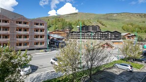 A modern building with a unique facade, a parking area with cars, and traditional wooden buildings in the background. - Flat with a balcony near the slopes (Les Deux Alpes)
