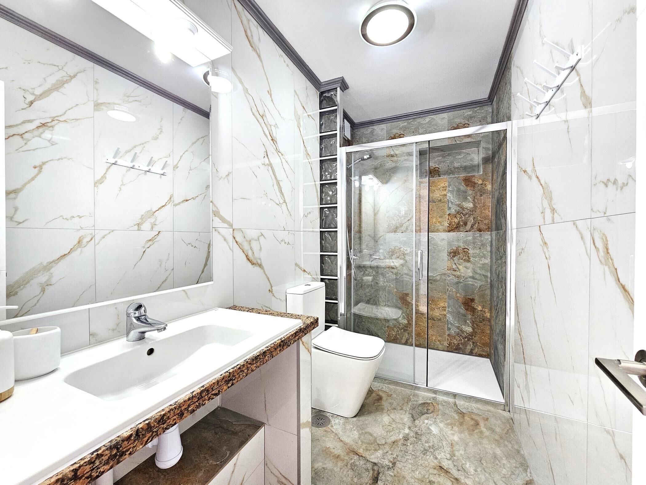 Een moderne badkamer met een marmeren wastafelmeubel, een douchecabine van glas en een toilet.