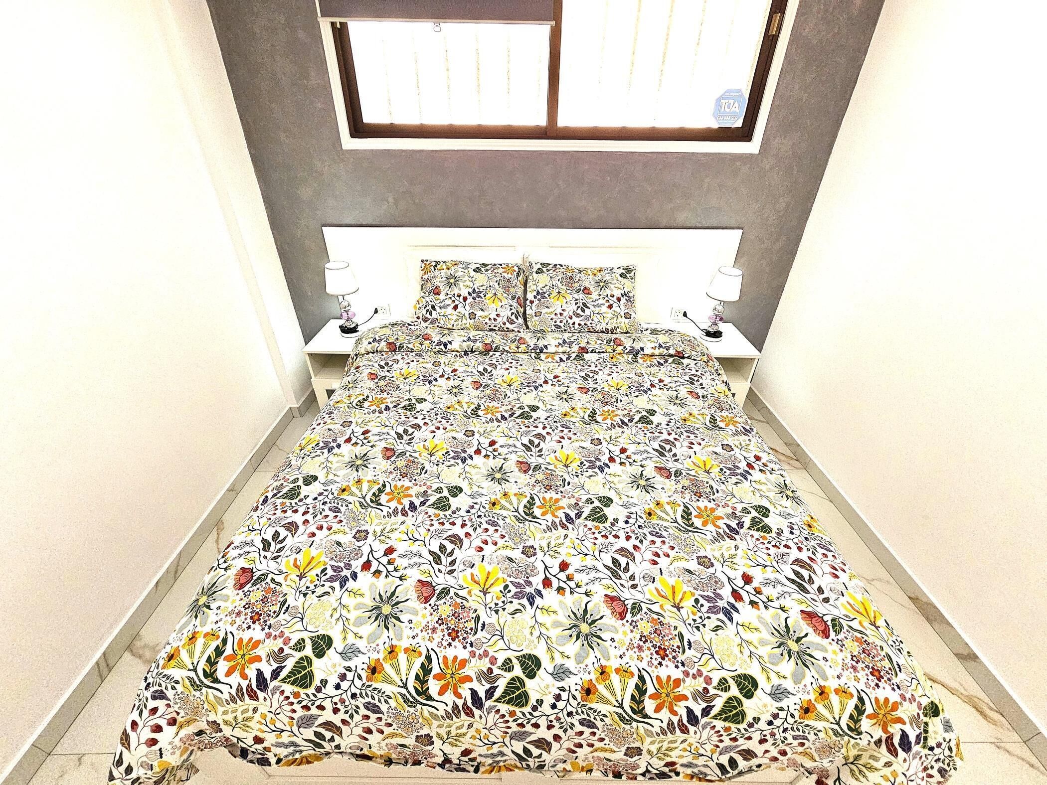 A bed with a floral bedspread, two bedside tables with lamps, and a window above the bed.