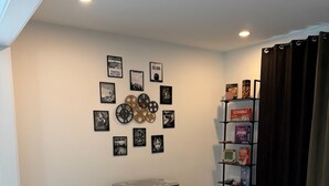 Un salon comprenant une table de jeux, deux chaises, un tapis à motifs, un mur orné de tableaux et une étagère remplie de jeux de société.