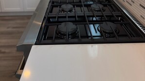 Une cuisine avec des armoires blanches, une cuisinière en acier inoxydable et un panier de fruits posé sur le comptoir.