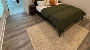 Une chambre à coucher comprenant un lit, un ventilateur de plafond, une table de chevet, un tableau accroché au mur et une fenêtre avec des stores.