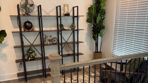 Un escalier avec une rampe en bois et des balustres noires, menant à un palier où se trouve une étagère en métal noir, sur laquelle sont exposés divers objets décoratifs.