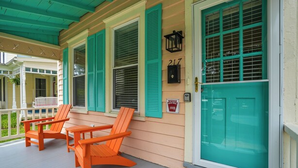 A porch with two orange Adirondack chairs, a teal door, and a window with shutters.