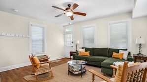 A living room with a green sofa, wooden chairs, a coffee table, and a ceiling fan.