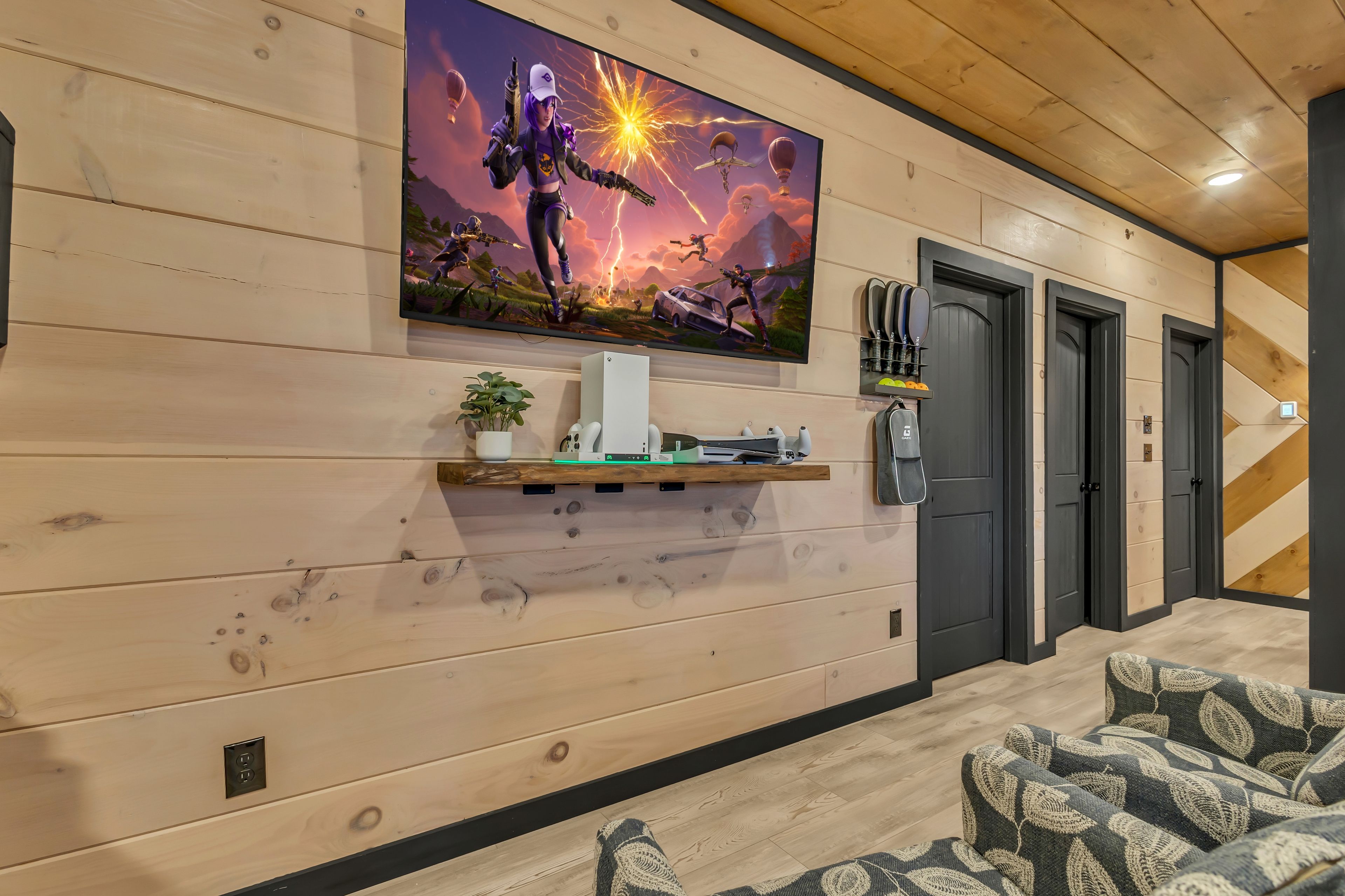 Un intérieur moderne avec un mur en bois, un téléviseur fixé au mur diffusant un match, une étagère contenant des appareils électroniques et une porte.