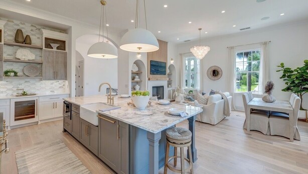 Una cocina moderna con una isla de mármol, luces colgantes y una zona de comedor con mesa y sillas.