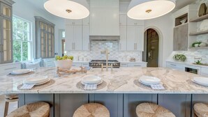 Una cocina amplia con una isla grande, muebles color blanco e iluminación colgante.