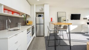 A modern kitchen with white cabinets, a stainless steel refrigerator, and a wooden dining table with bar stools.