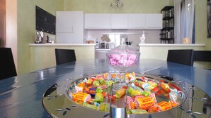 A dining table with a glass centerpiece and various candies. The room has white cabinets and a chandelier. - ☀️🌳🏡🦔Dimora del Riccio (Bergamo)