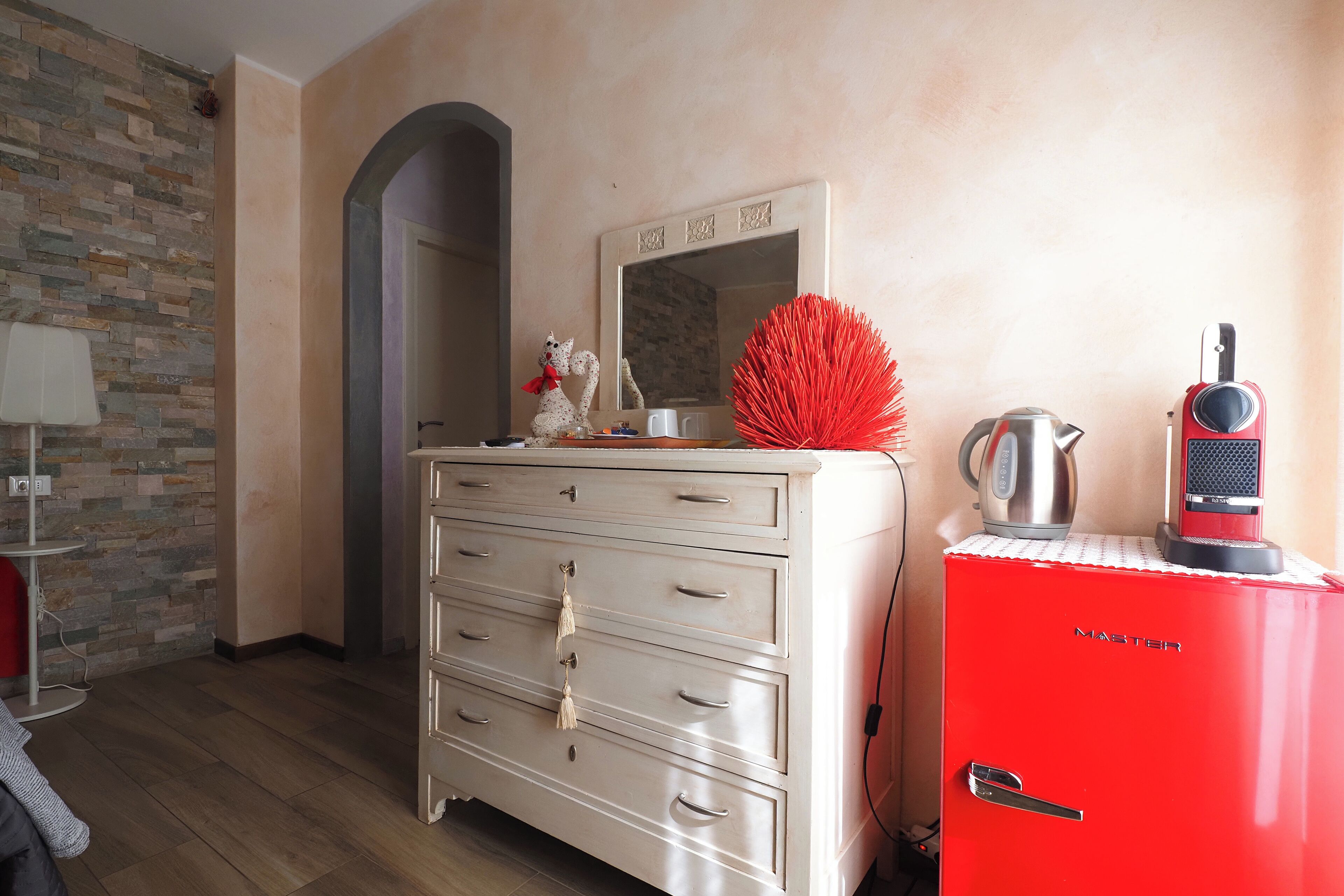 A room with a stone-patterned wall, a white dresser with drawers, a red cabinet, and a mirror above the dresser.
