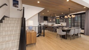 A modern kitchen with wooden flooring, a dining area with a large table and chairs, and a staircase with patterned carpet.