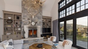 A modern living room with a stone fireplace, a large window with a mountain view, and a cozy seating area.
