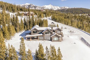 Een modern skigebied-lodge met meerdere gastenkamers, een skilift en uitzicht op de omliggende besneeuwde bergen.
