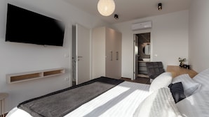 A modern bedroom with a flat-screen TV, a large bed with a white and black duvet, a grey throw, and a wooden nightstand with a small plant. - Villa Villa Mattia (Istria - Novigrad) (Novigrad)