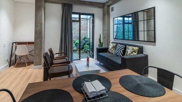 Una sala de estar moderna con un sofá, sillas, una mesa de centro y una mesa de comedor. Hay un ventanal con vistas a la vegetación exterior.