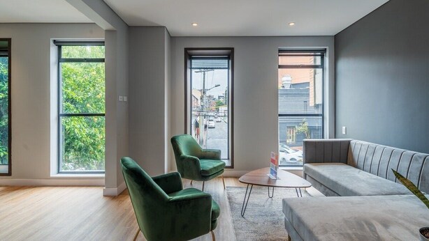 Ein modernes Wohnzimmer mit großen Fenstern, einem grauen Sofa und zwei grünen Sesseln.