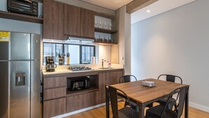 Eine moderne Küche mit Holzausstattung, einem Edelstahlkühlschrank, einer eingebauten Mikrowelle und einem Essbereich mit einem Holztisch und schwarzen Stühlen.
