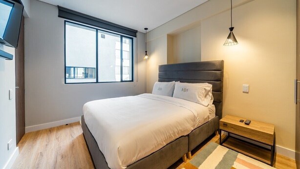 Ein modernes Schlafzimmer mit einem großen Bett, einem Fenster, einem Nachttisch und einer Hängeleuchte.