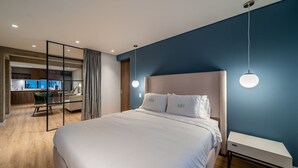 A modern hotel room with a large bed, a bedside table, and a view of the kitchen area.