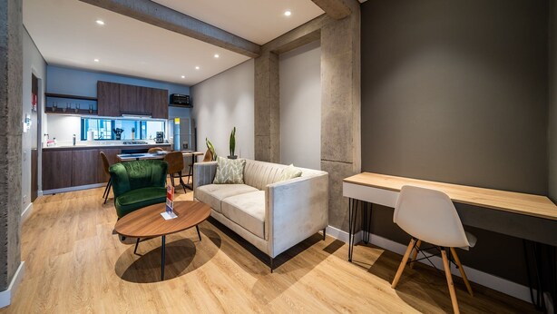 A modern living room with a sofa, a green armchair, a wooden coffee table, and a dining table with chairs.