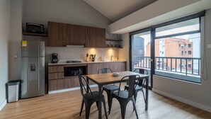 Cozinha moderna com armários de madeira, uma geladeira de aço inoxidável, fogão a gás e área de refeições com mesa de madeira e cadeiras pretas.