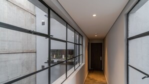 Um corredor estreito com janelas amplas em ambos os lados, parede de concreto à esquerda e uma porta no final.