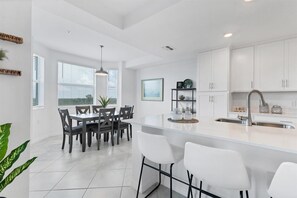 A modern kitchen with white cabinetry, a central island with bar stools, and a dining area with a table and chairs.