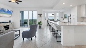 A modern kitchen with a central island, a dining area with chairs, and a balcony with a view.