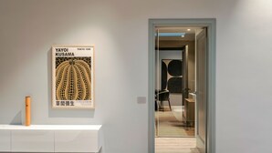 A minimalist interior with a framed artwork on the wall, a white console table, and a doorway leading to another room. - Attico 56 (Brescia)