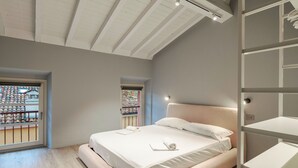 A modern bedroom with a large bed, built-in shelving, and a view through a window. - Attico 56 (Brescia)