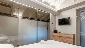 Quarto de hotel com uma cama grande, cabeceira de madeira, televisão fixada na parede e armário com portas de correr.