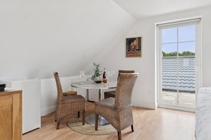 Un coin repas avec une table ronde, des chaises en osier, un tableau au mur et une vue à travers une porte coulissante.