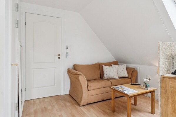 Ein Zimmer mit einem braunen Sofa, einem Holztisch, einer weißen Tür und einer schrägen Decke.