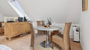 A dining area with a round table, wicker chairs, a kitchen in the background, and a ceiling skylight. - Talian charm at VINEYARD near Karrebæksminde (Karrebæksminde)