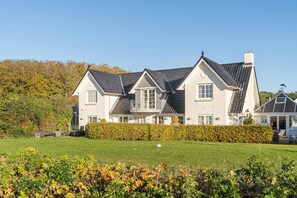 Ein großes, zweistöckiges Haus mit symmetrischer Gestaltung, einem gepflegten Rasen und einer Hecke im Vordergrund.