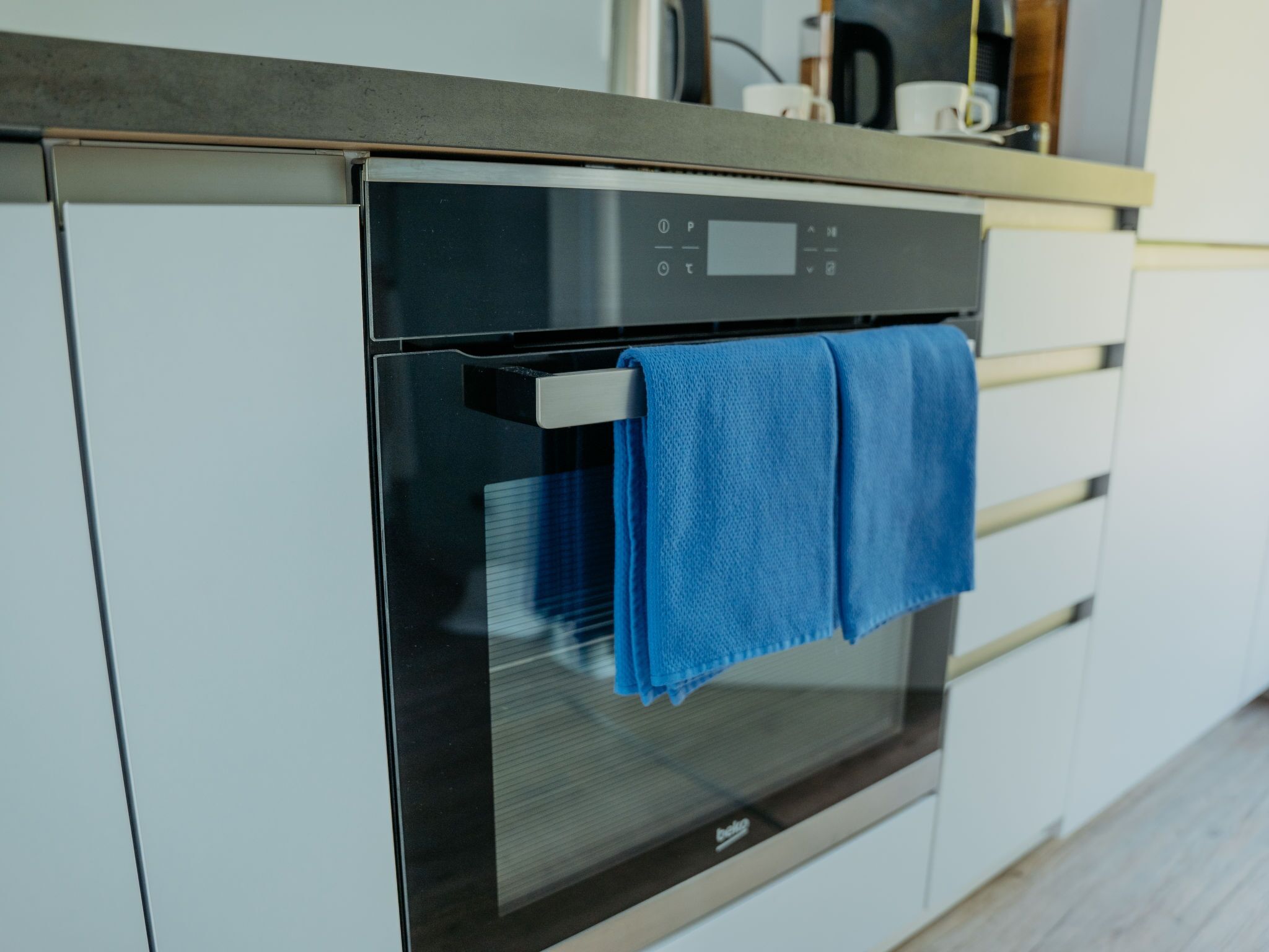Moderni keittiö, jossa on sisäänrakennettu uuni ja sininen pyyhe roikkuu uunin oven kahvassa.