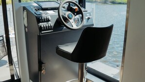 A modern control station with a steering wheel, a chair, and a view of a lake through large windows. - Floating Home-Hausboot Saarschleife by Interhome (Mettlach)