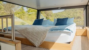 A modern bedroom with a bed, pillows, and a view of greenery outside. - Floating Home-Hausboot in Merzig liegend by Interhome (Merzig)