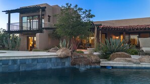 A modern house with a pool, large rocks, and cacti.