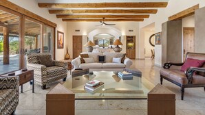 A spacious living area with a glass coffee table, sofas, and wooden beams on the ceiling.