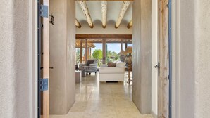A hallway with a wooden ceiling, a white door, and a view into a living area with a sofa and a lamp.
