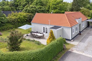 A two-story house with a red-tiled roof, a covered patio with outdoor furniture, and a well-maintained garden.