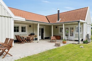 A covered outdoor patio with wooden furniture, a chimney, and a garden area.