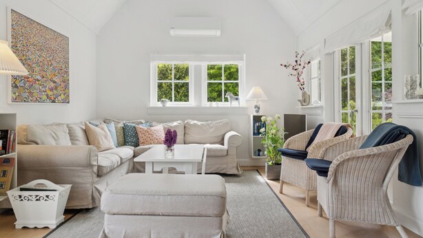 A spacious living room with a white sofa, a coffee table, wicker chairs, and a large window with a view of greenery. - Renovated summer house in Vejby/ Tisvilde (Vejby)